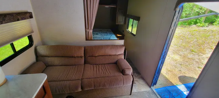 Inside an rv rental: a comfortable sofa, bunk bed, and open door showing outside. Bright and spacious camper interior.. Jayco Jay Flight SLX 2015