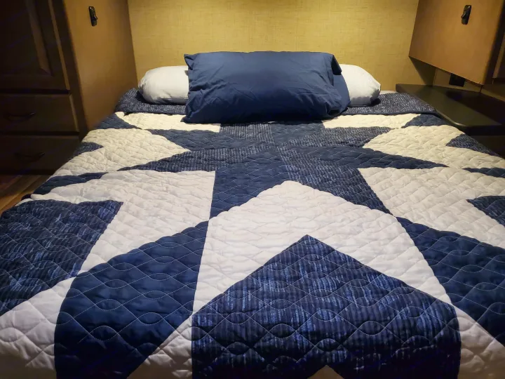 Cozy bed with a striking blue and white star-patterned quilt, perfect for an RV rental adventure.. Thor Majestic 2019