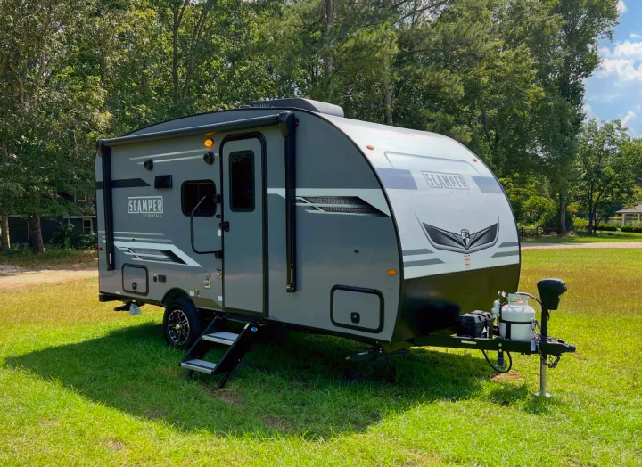 A modern grey and white SCAMPER travel trailer RV rental, parked on green grass with trees in the background, ready for adventure.. Venture Rv Sonic 2023