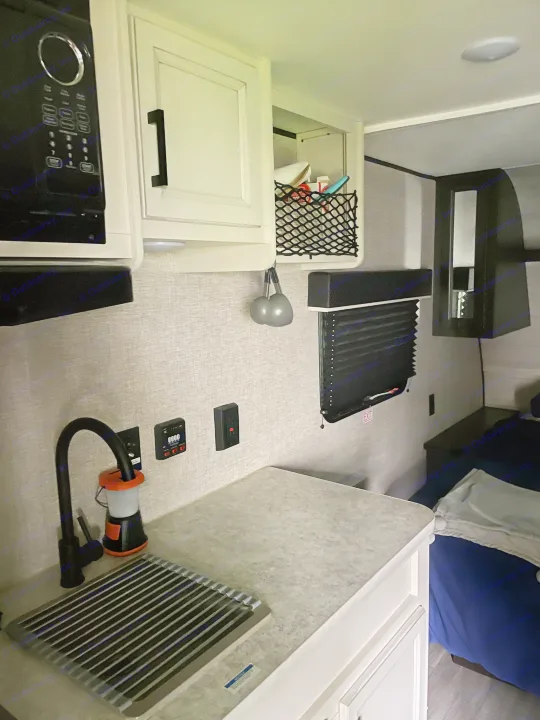 Compact RV rental interior featuring a kitchen with microwave, sink, controls, storage, and adjacent sleeping space.. Jayco Jay Flight SLX 2022