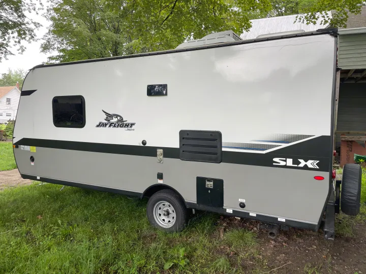 Side view of a white and gray Jayco Jay Flight SLX travel trailer, perfect for an RV rental. Visible utility access & tire.. Jayco Jay Flight SLX 2022