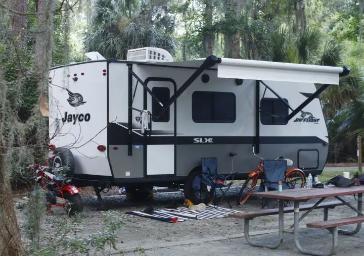 A Jayco RV rental at a serene campsite with an extended awning, picnic table, bike, and mini-bike. Perfect outdoor travel trailer setup.. Jayco Jay Flight SLX 2022