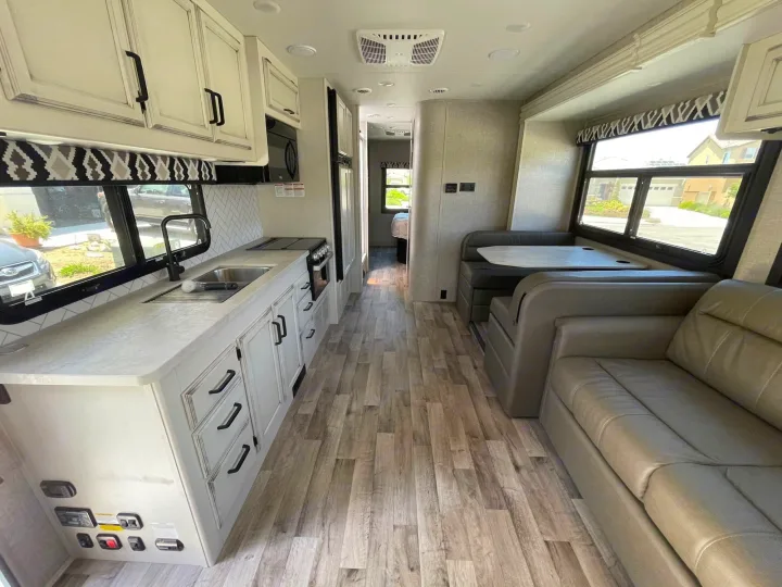 Modern RV rental interior: kitchen with light cabinets, dinette, and sofa. Perfect for your travel adventures.. Jayco Greyhawk 2022