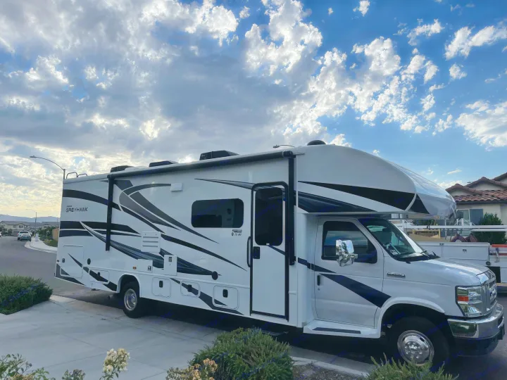 Ready for adventure! This white Jayco Greyhawk RV rental with black graphics is parked roadside under a beautiful cloudy sky.. Jayco Greyhawk 2022