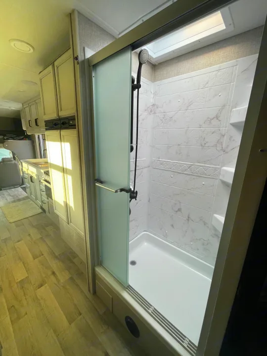 RV rental interior: a modern shower with a sliding door on the right, and a bright kitchen with light cabinets on the left.. Jayco Greyhawk 2022