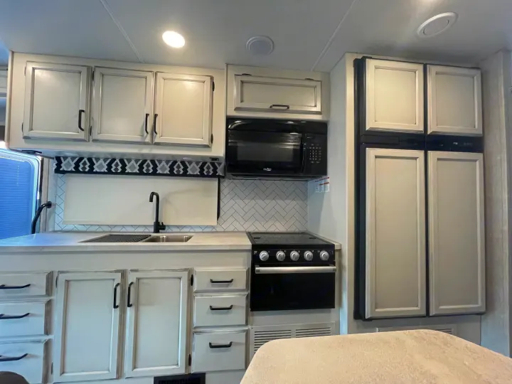 Modern RV rental kitchen interior: light cabinets, black microwave, stove, sink, and full-size fridge. Ready for adventure!. Jayco Greyhawk 2022