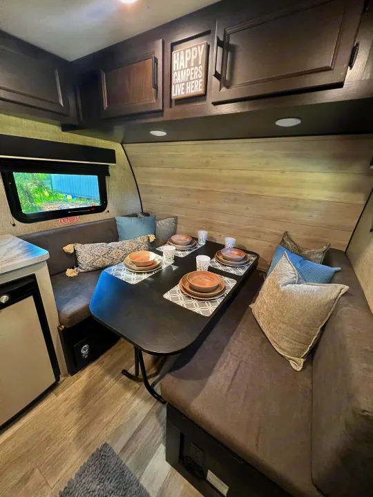 An inviting RV rental interior: a cozy dining area with a dark table set for meals, plush benches, and overhead cabinets.. Jayco Jay Flight SLX Baja Edition 2023