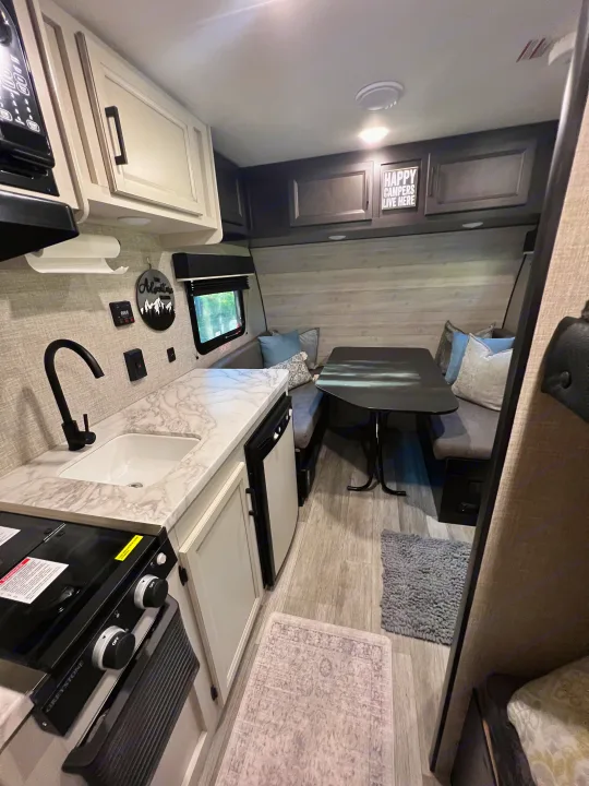 Bright and functional RV rental interior featuring a compact kitchen with stove, sink, fridge, and a cozy dining booth.. Jayco Jay Flight SLX Baja Edition 2023
