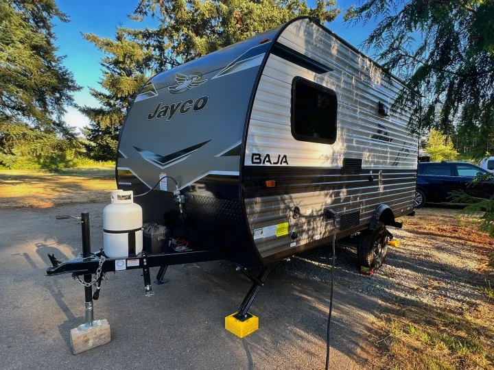 A modern gray and black Jayco Baja travel trailer, ideal for an rv rental, is parked and set up at a sunny campsite.. Jayco Jay Flight SLX Baja Edition 2023
