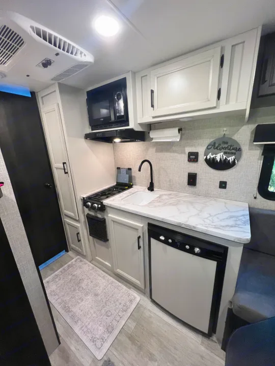 A well-equipped, bright RV rental kitchen, featuring a microwave, stove, sink, and refrigerator, for comfortable travels.. Jayco Jay Flight SLX Baja Edition 2023