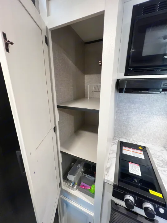 RV rental kitchen: An open pantry with shelves, next to a microwave and stovetop, offering convenient storage.. Jayco Jay Flight SLX Baja Edition 2023