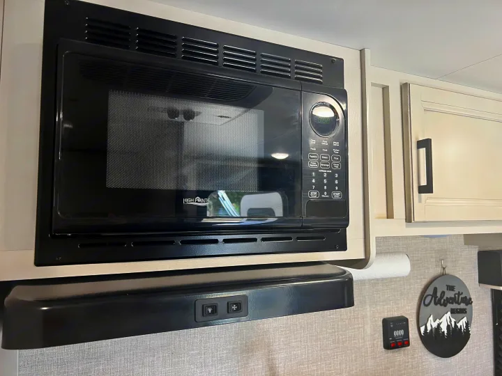 High Pointe microwave and range hood in a modern RV rental kitchen, featuring light cabinets and wall decor.. Jayco Jay Flight SLX Baja Edition 2023