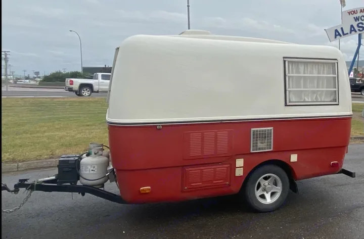 A charming retro red and white travel trailer RV rental, with a propane tank, sits on pavement.. Trillium Rv other 1975
