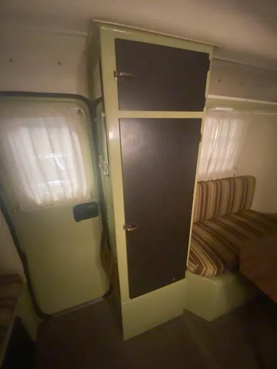 RV rental interior: light green overhead cabinets with dark doors, striped seating, and white curtains on a window.. Trillium Rv other 1975