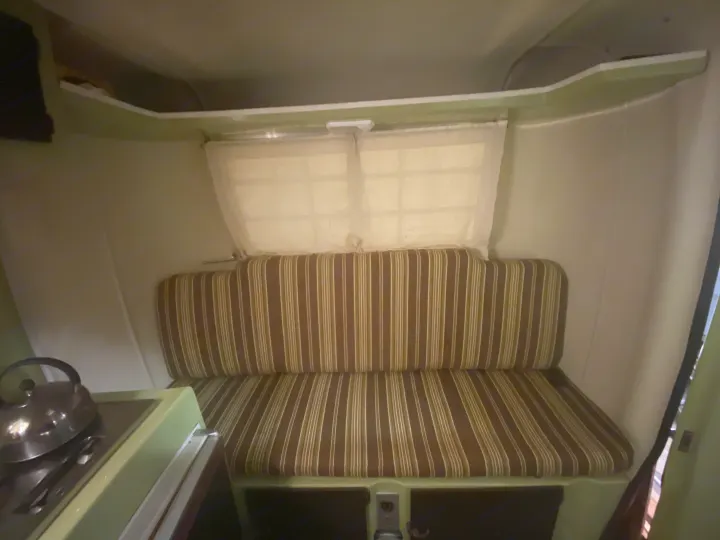 Inside a charming RV rental, featuring cozy striped bunk seating, windows, a storage shelf, and a compact kitchenette.. Trillium Rv other 1975