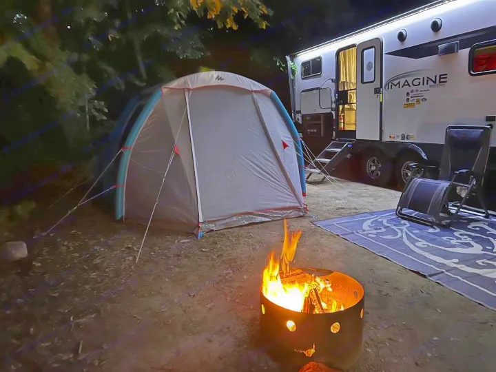 Night camping scene with illuminated RV rental, cozy tent, and warm bonfire. Perfect outdoor escape under the stars.. Grand Design Imagine 2023