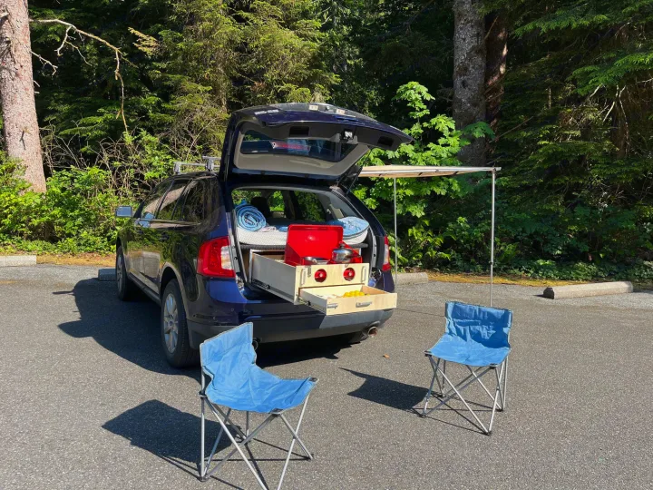 Blue car converted for camping with pull-out kitchen, bed, and awning. An RV rental alternative for outdoor adventures.. Ford Edge 2011