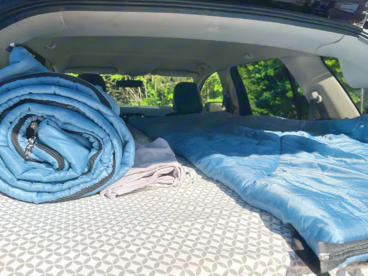 Cozy car camping setup for your next RV rental road trip. Blue sleeping bags on a patterned mattress inside an SUV.. Ford Edge 2011