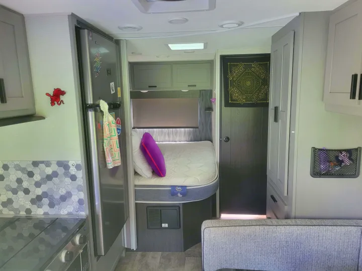 RV rental interior featuring a compact kitchen with fridge, hexagon backsplash, comfortable bed, and storage options.. Solera Solera Motorhome 2022
