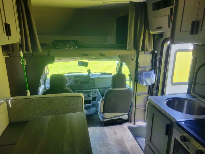 Inside this **rv rental**: a cozy dinette, well-equipped kitchen, driver's cockpit, and an over-cab bunk area for guests.. Solera Solera Motorhome 2022