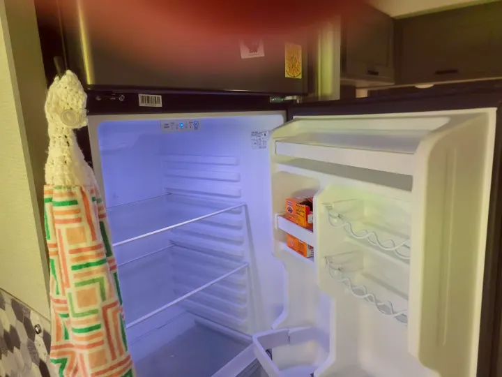 This RV rental's compact refrigerator stands open, showcasing its clean interior with shelves and a few baking soda boxes.. Solera Solera Motorhome 2022