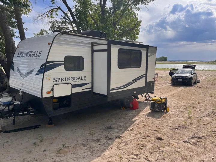 Lakeside RV rental camping setup: a white travel trailer, open slide, generator, and car on sand.. Keystone RV Springdale 2022