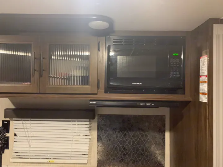 Compact RV rental kitchen features overhead cabinets, microwave, range hood, and window blinds.. Forest River Cherokee Grey Wolf 2020