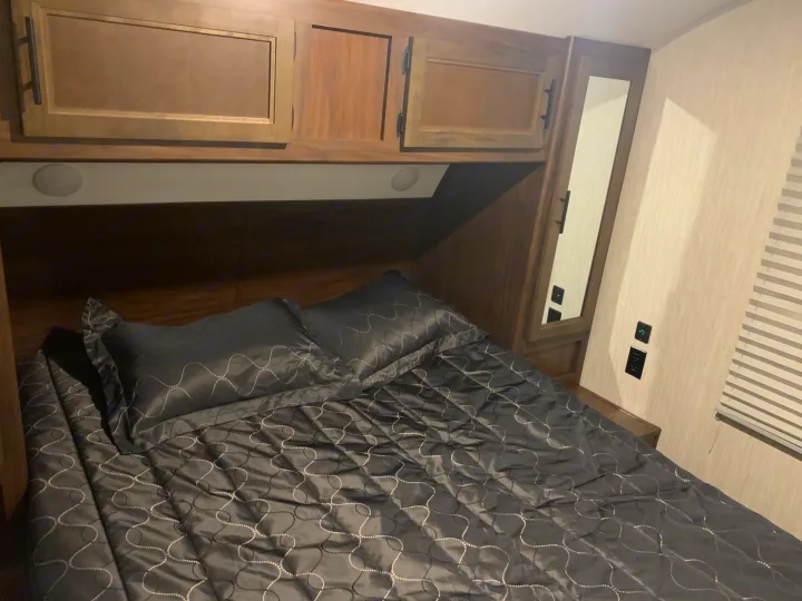 Cozy RV rental bedroom with dark patterned bedding, built-in storage cabinets, and wall mirror. Ideal for travel.. Forest River Cherokee Grey Wolf 2020