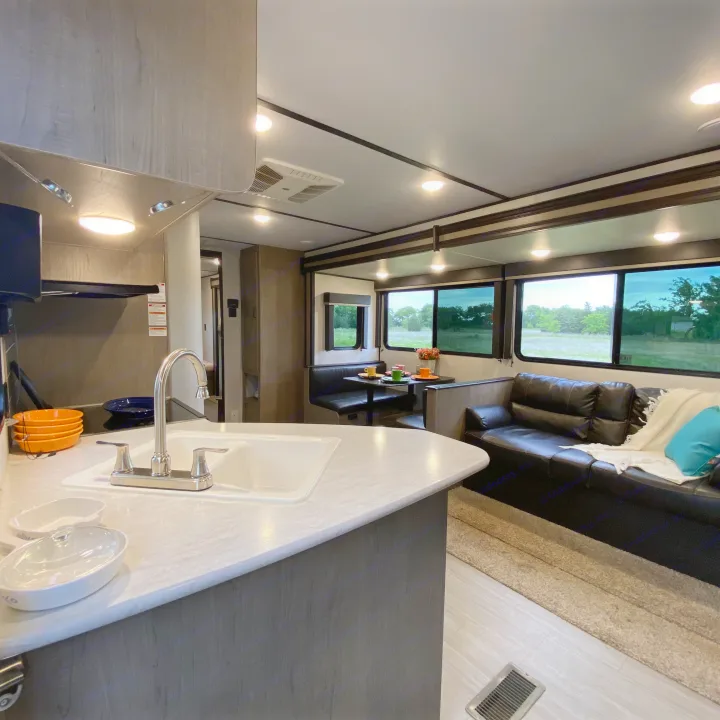 Spacious RV rental featuring a modern kitchen, dining booth, and living area with bright views of nature.. Keystone Hideout 2021