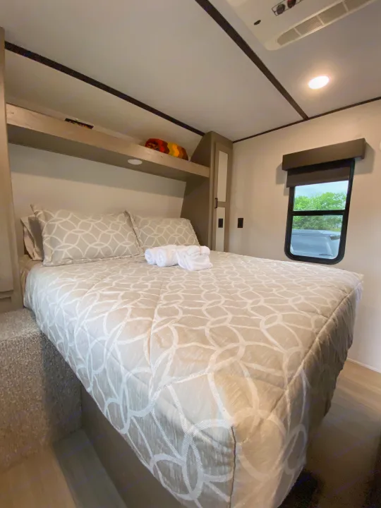 Cozy and comfortable RV rental bedroom featuring a patterned bedspread, pillows, and convenient overhead storage.. Keystone Hideout 2021