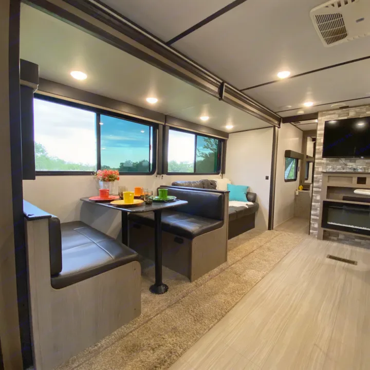 Cozy RV rental interior featuring a dinette with bench seating, a living area with sofa and TV/fireplace, and large windows.. Keystone Hideout 2021