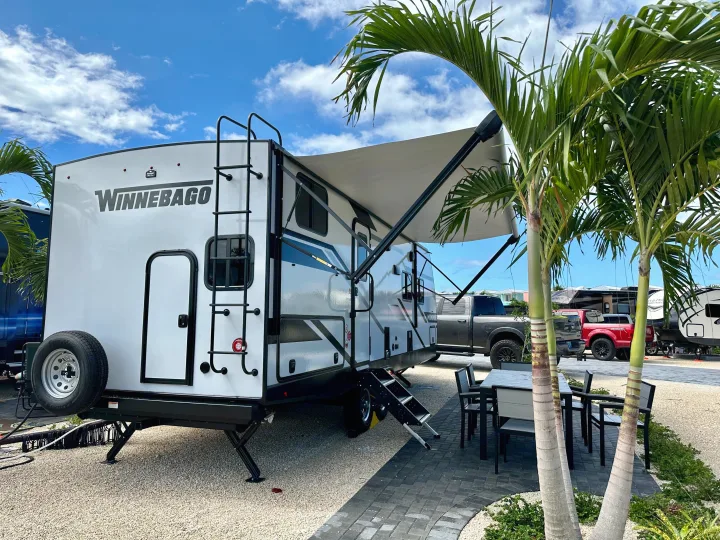 A white Winnebago RV trailer with an extended awning and outdoor dining area at a sunny resort, ideal for an RV rental getaway.. Winnebago Minnie 2301BH 2023