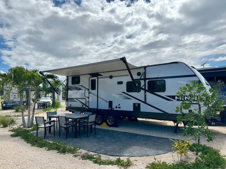 Your RV rental getaway: a travel trailer with an extended awning, patio, and outdoor dining set at a resort campsite.. Winnebago Minnie 2301BH 2023