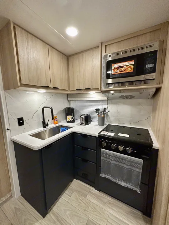 Modern, compact kitchen in an RV rental, complete with sink, microwave, and stove, ideal for on-the-go cooking.. Winnebago Minnie 2301BH 2023