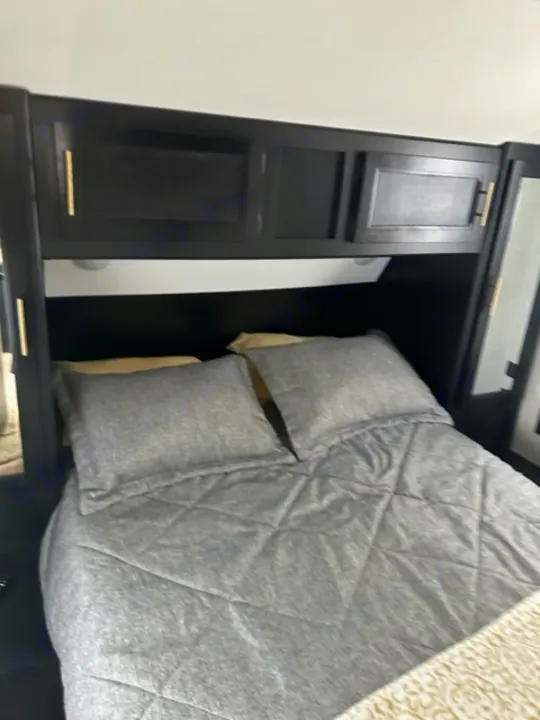 Compact RV rental bedroom with black built-in storage cabinets and cozy grey bedding, optimizing space for travel.. Forest River Cherokee 2022
