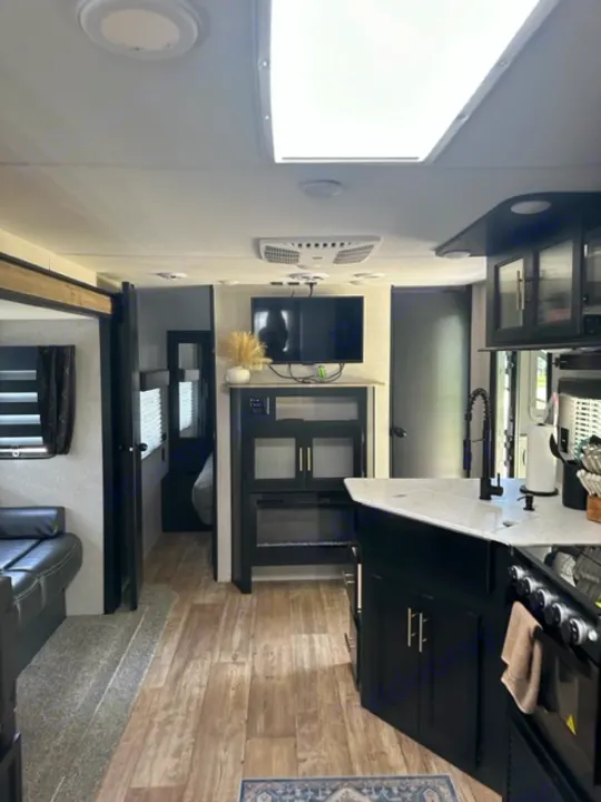 Spacious RV rental interior featuring a sleek black kitchen, comfy living area, wood floors, and bright natural light.. Forest River Cherokee 2022