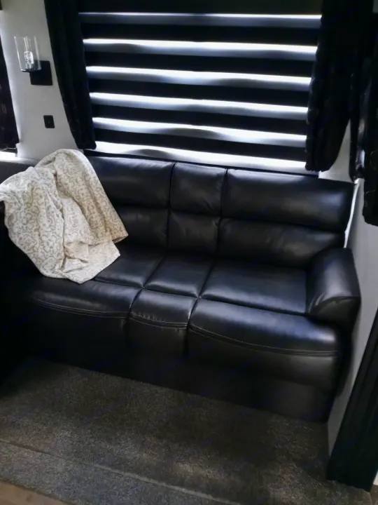 Comfortable RV rental living area featuring a black sofa with a patterned blanket, striped window blinds, and carpeted floor.. Forest River Cherokee 2022