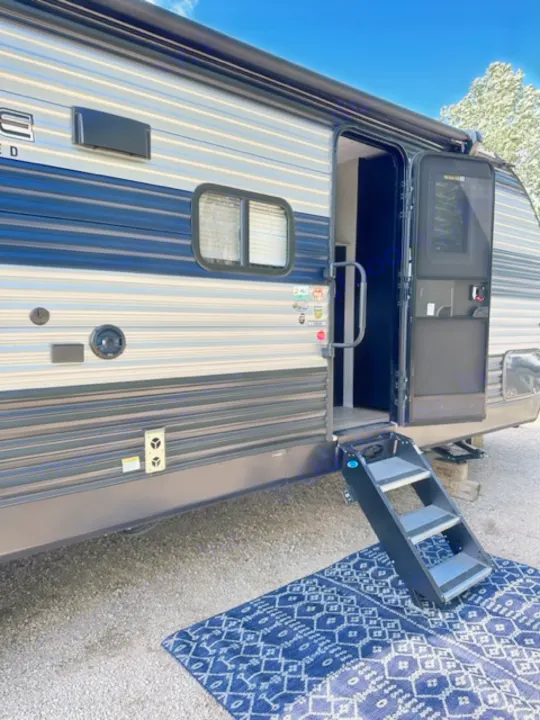 RV rental showing a striped travel trailer with its door open, revealing interior steps leading to an outdoor rug.. Forest River Cherokee 2022