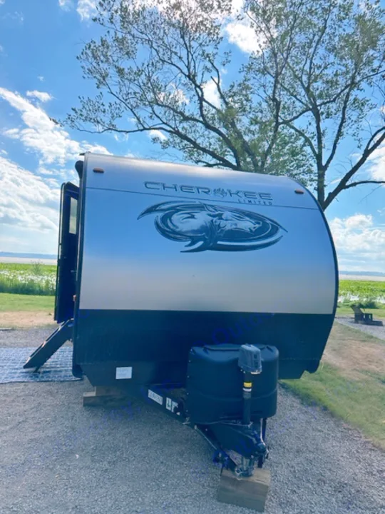 RV rental: A white and black Cherokee Limited travel trailer parked on gravel, with tree branches and a blue sky overhead.. Forest River Cherokee 2022