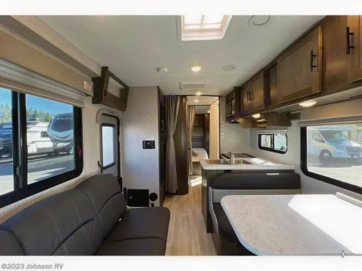 Inside this RV rental: View of the living area with a dark sofa, kitchen with sink, dinette, and hallway to the bedroom.. Coachman Leprechaun 2022