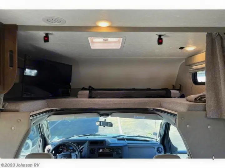 Spacious RV rental interior featuring a cab-over bunk bed with a TV, dashboard below, and cozy amenities.. Coachman Leprechaun 2022