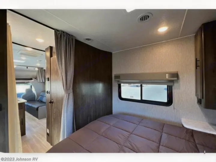 RV rental interior: bedroom with bed and window, separated by a privacy curtain from the living area with a sofa.. Coachman Leprechaun 2022