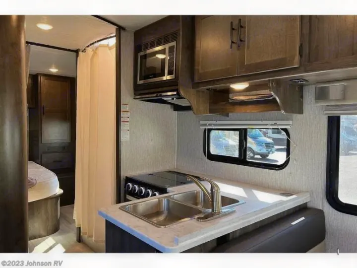 RV rental: Inside, a compact kitchen with sink/stove, dining area, and a bed behind a privacy curtain.. Coachman Leprechaun 2022