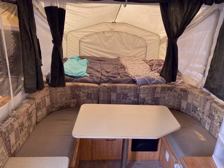 Interior view of an rv rental pop-up camper, showing the bed and dinette area with patterned cushions and a table.. Palomino Yearling 2012