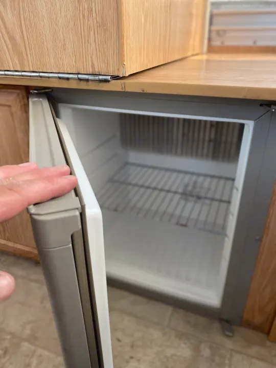 Hand opening a compact RV rental fridge, built into wood cabinetry with wire shelves visible inside.. Palomino Yearling 2012