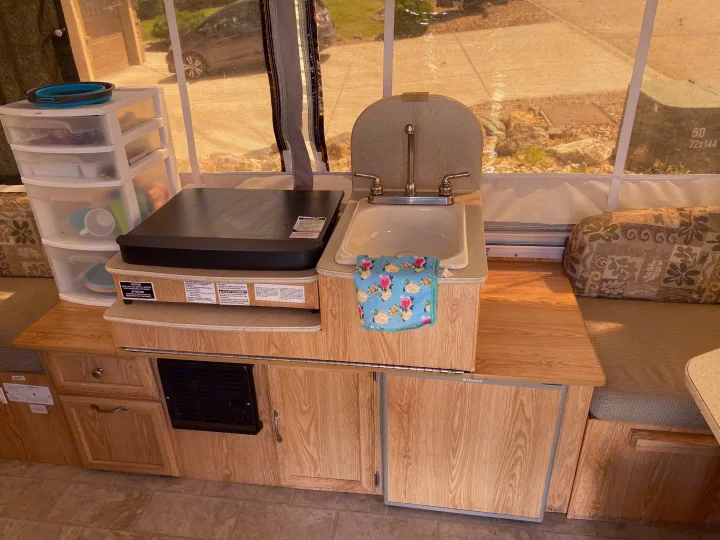 RV rental kitchen setup with sink, stovetop, and clear storage bins.. Palomino Yearling 2012