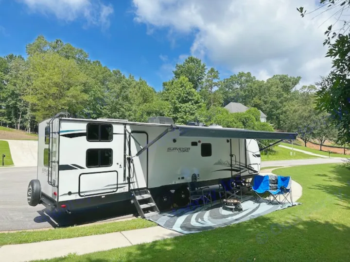 This RV rental is set up for a relaxing outdoor experience, with chairs and a fire pit on a mat next to the travel trailer.. Forest River Surveyor Legend 2022