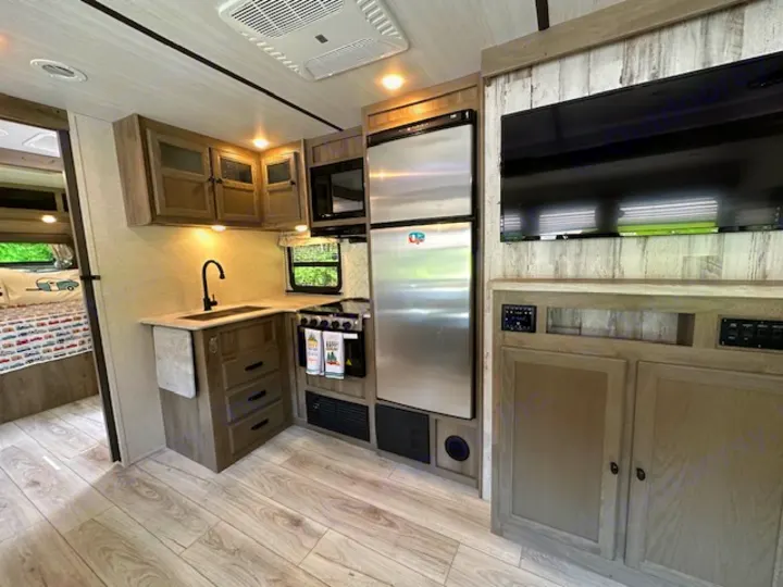 Spacious, modern rv rental interior showcasing a bright kitchen, living area with TV, and a glimpse of the cozy bedroom.. Forest River Surveyor Legend 2022