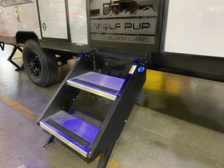 This Wolf Pup travel trailer RV rental, parked indoors, shows its black access steps & wheel. Easy entrance for your next trip.. Forest River Cherokee Wolf Pup Black Label 2021