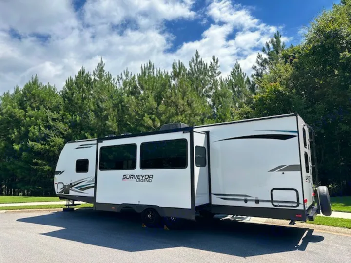 This sleek white Surveyor Legend travel trailer, ideal for an RV rental, is parked outdoors with trees under a blue sky.. Forest River Surveyor Legend 2022